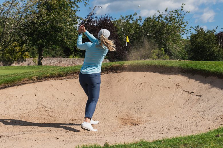 Female golfer hitting shot from bunker